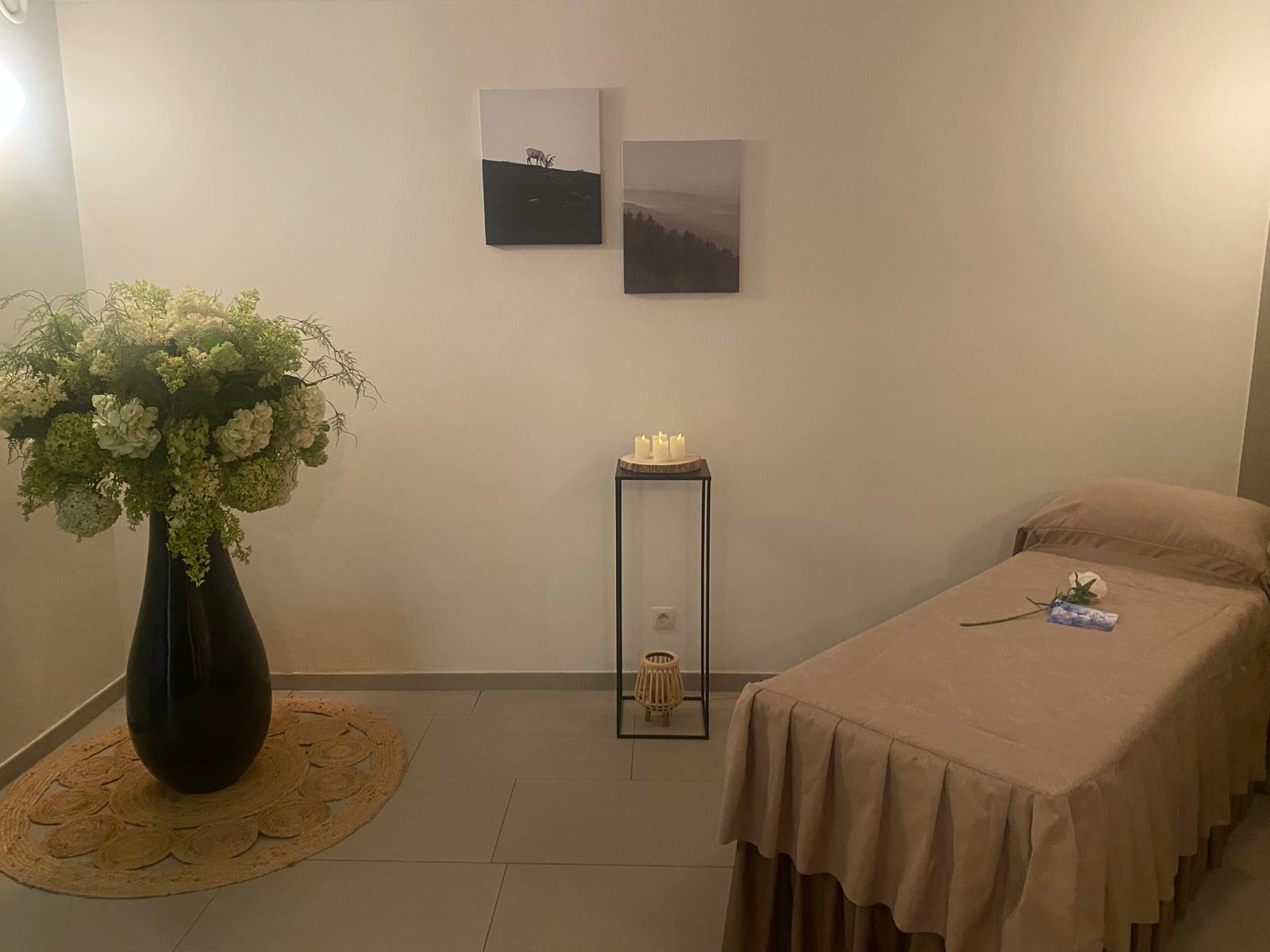 Groetkamer met beige ligbed, zacht licht en zwarte vaas met witte bloemen in de hoek